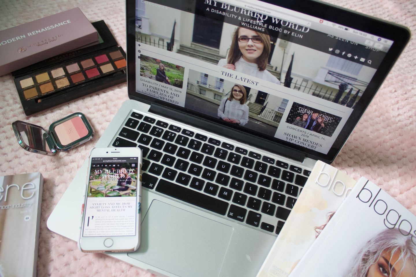 A photo of my blog's homepage on a macbook, there are a few issues of Blogsphere in the corner of the screen and an eyeshadow palette by Anastasia Beverly Hills on the other side of the laptop