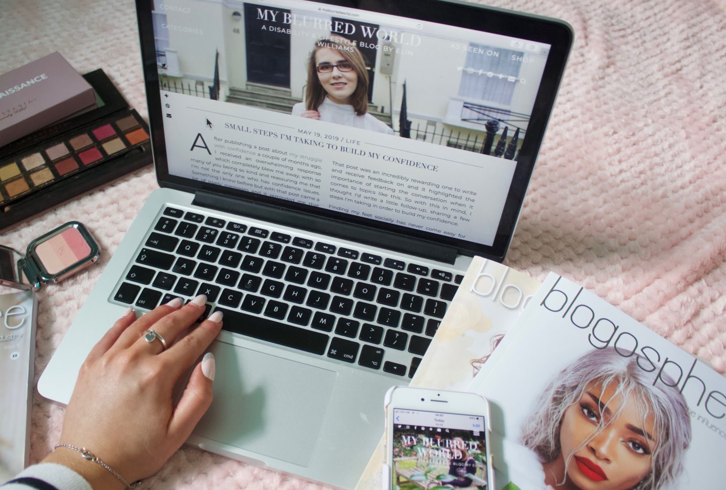 A photo of one of my blog posts showing on my laptop screen, my hand is on the keyboard as if I'm typing something