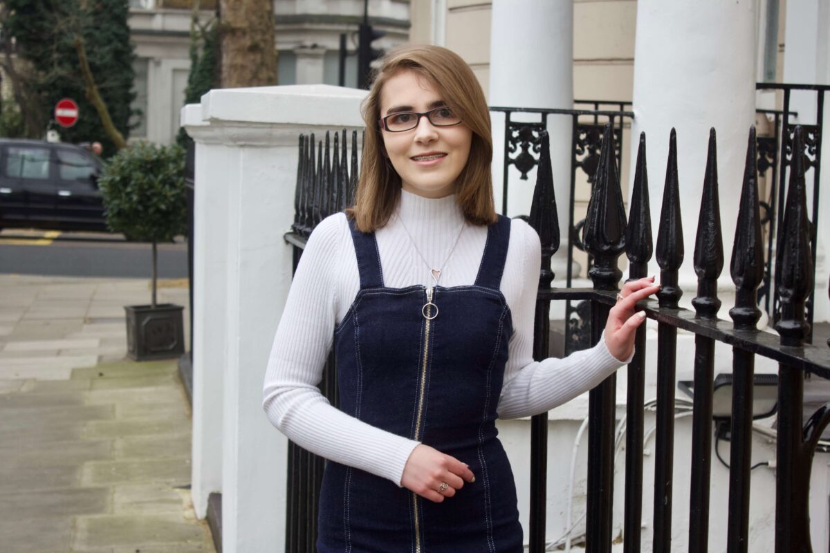 A photo of Elin smiling, her hand is on some pretty black railings outside a white house in London