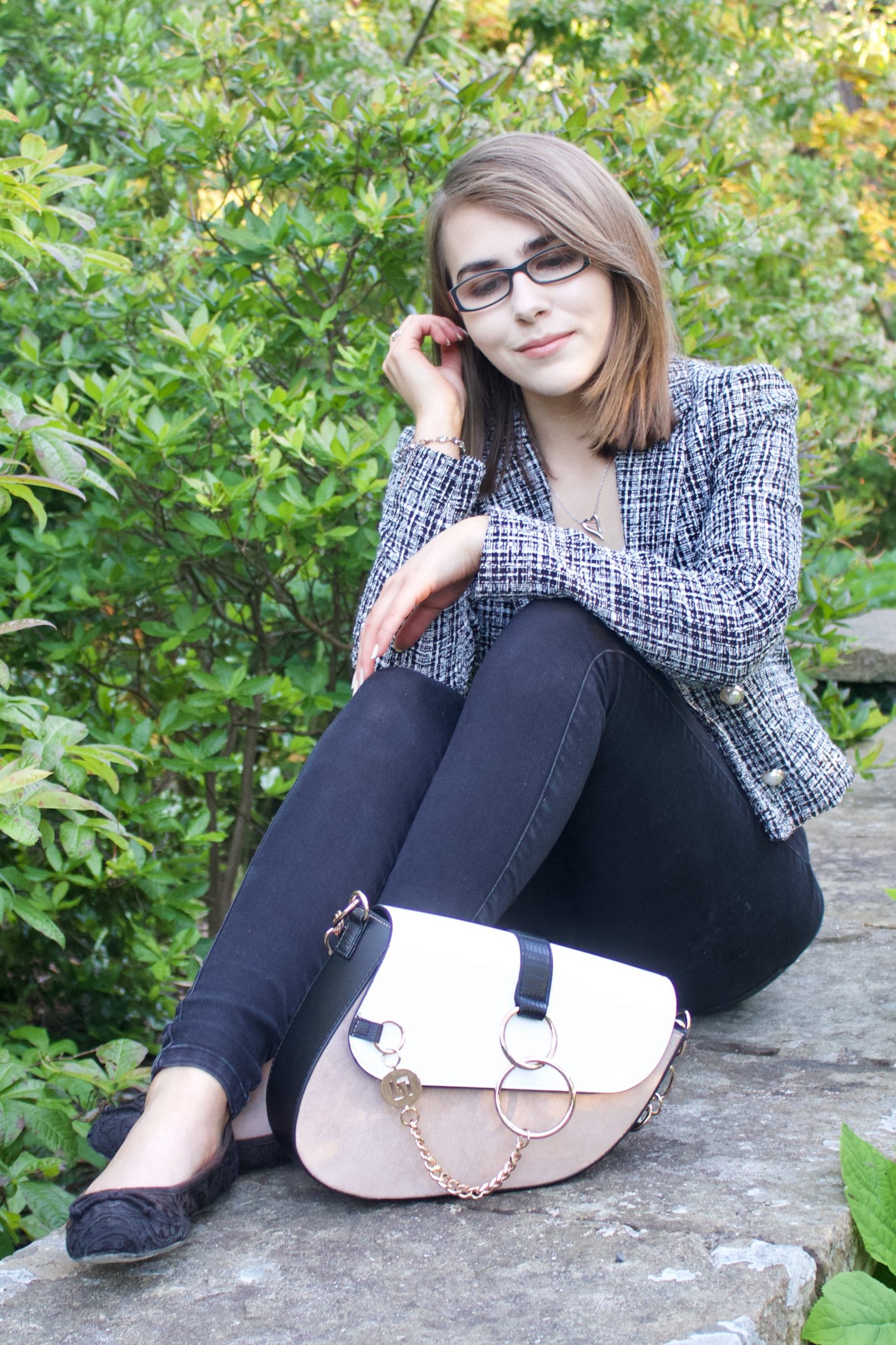 A photo of Elin sitting on a stone wall, she is looking down and her bag is placed in front of her