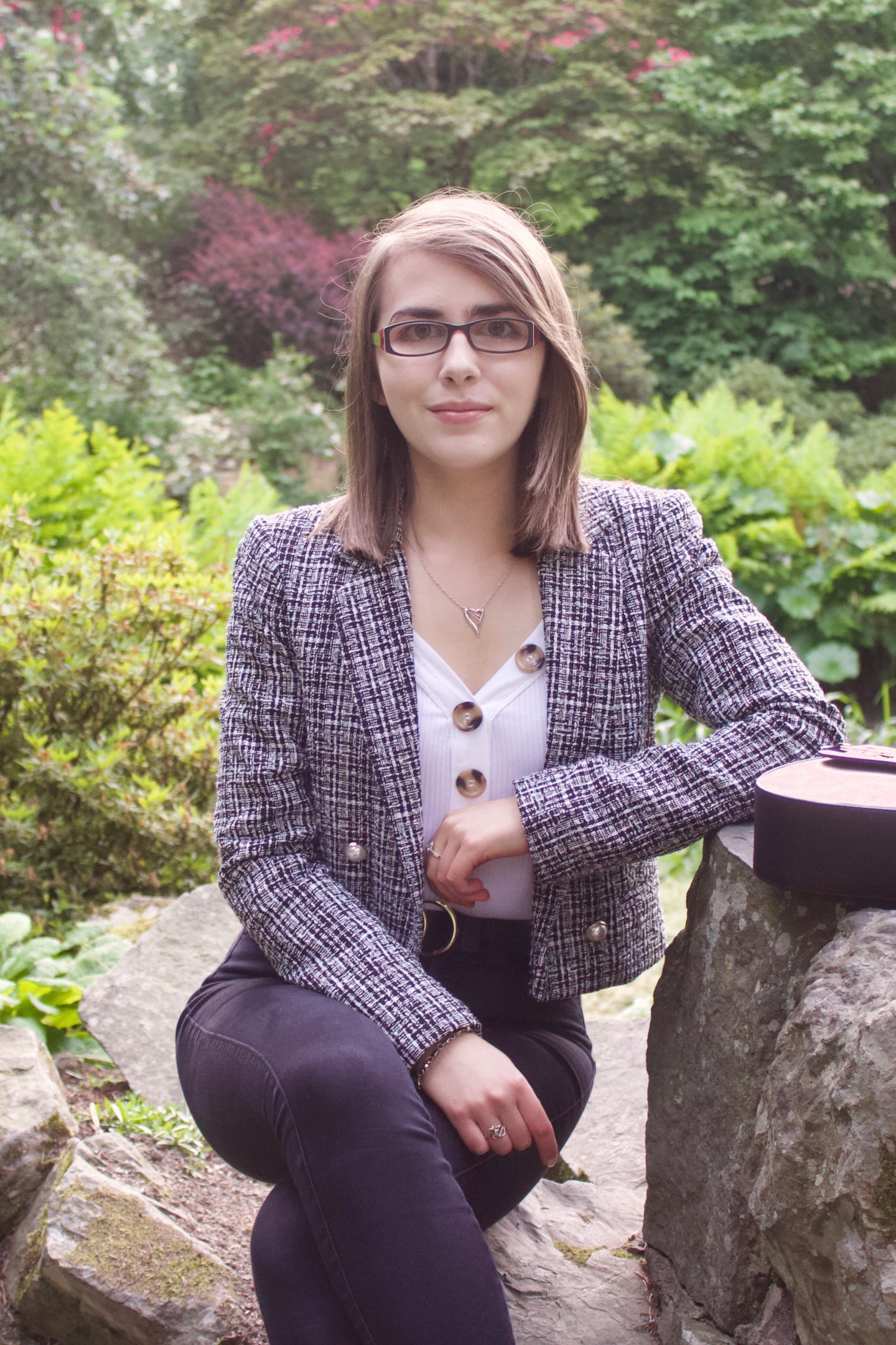 A photo of Elin sitting on a small rock whilst leaning against a bigger one which her bag is placed on