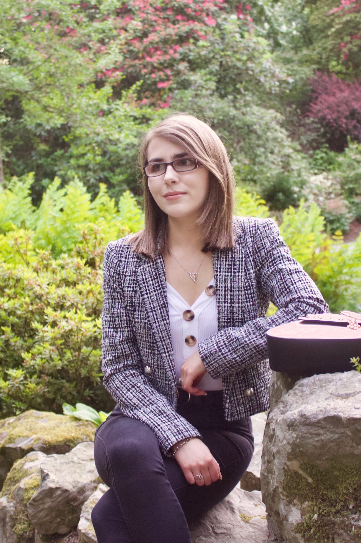 A photo of Elin sitting on a small rock whilst leaning against a bigger one which her bag is placed on, she is looking away from the camera