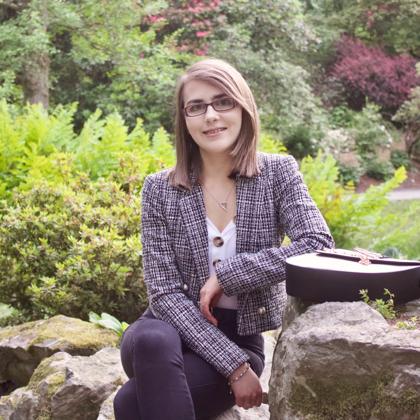 A photo of Elin in front of green plants and flowers, she is smiling at the camera
