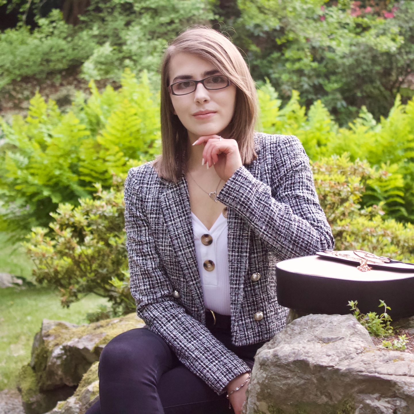 A photo of Elin sitting on a rock with her arm resting on the rock beside her which also has her bag on it