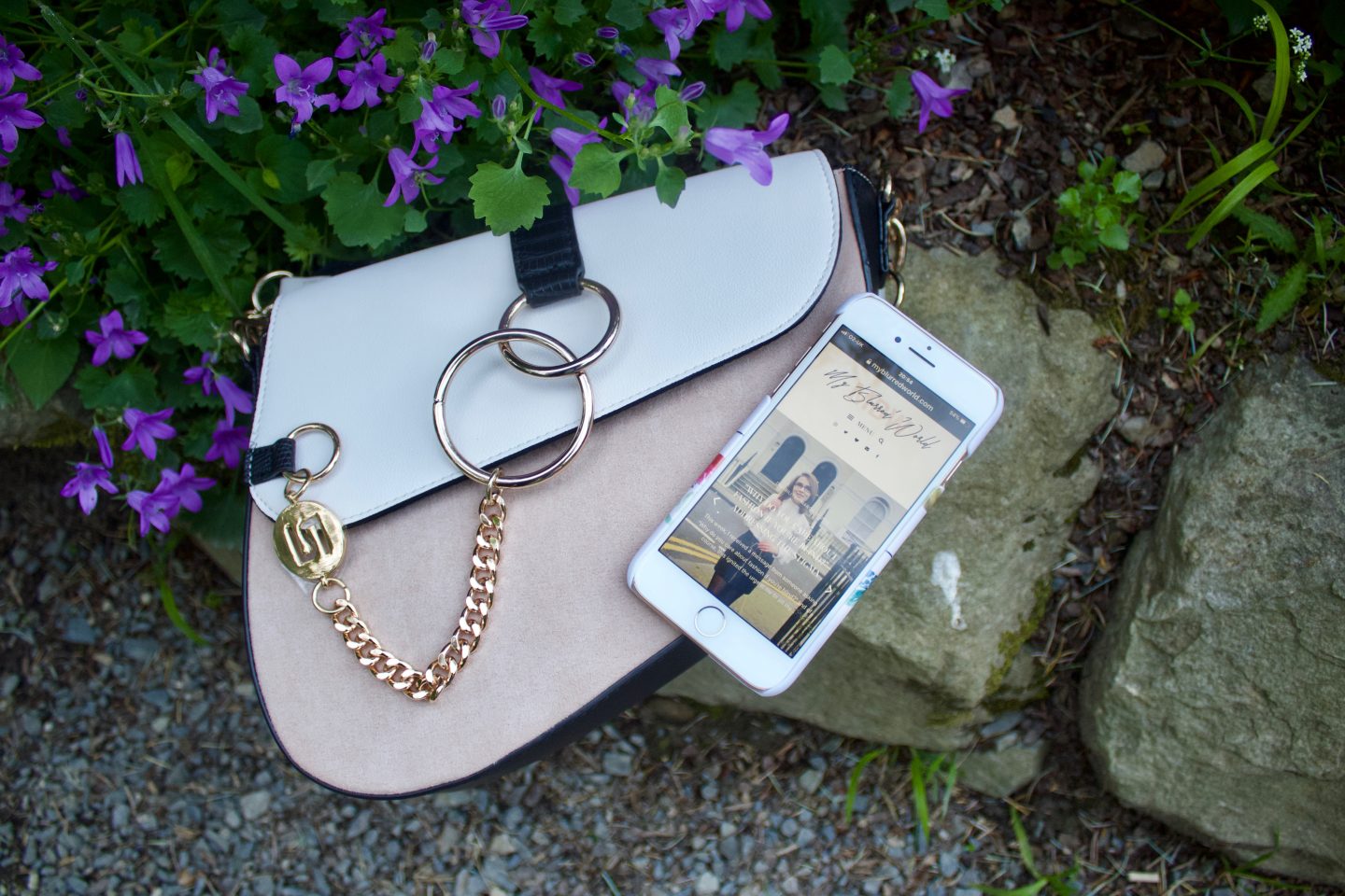 A photo of a white and beige saddle bag which has gold hardware, my phone is placed on it and the screen shows my blog's homepage