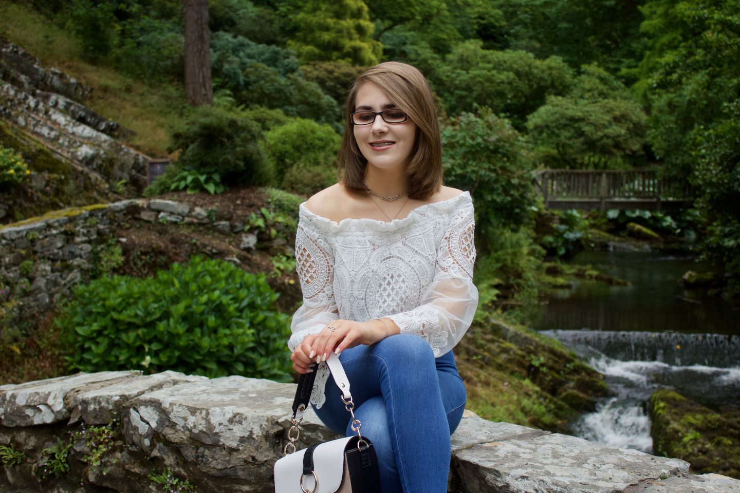 A photo of Elin sitting on a small stone bridge, she is smiling and looking down