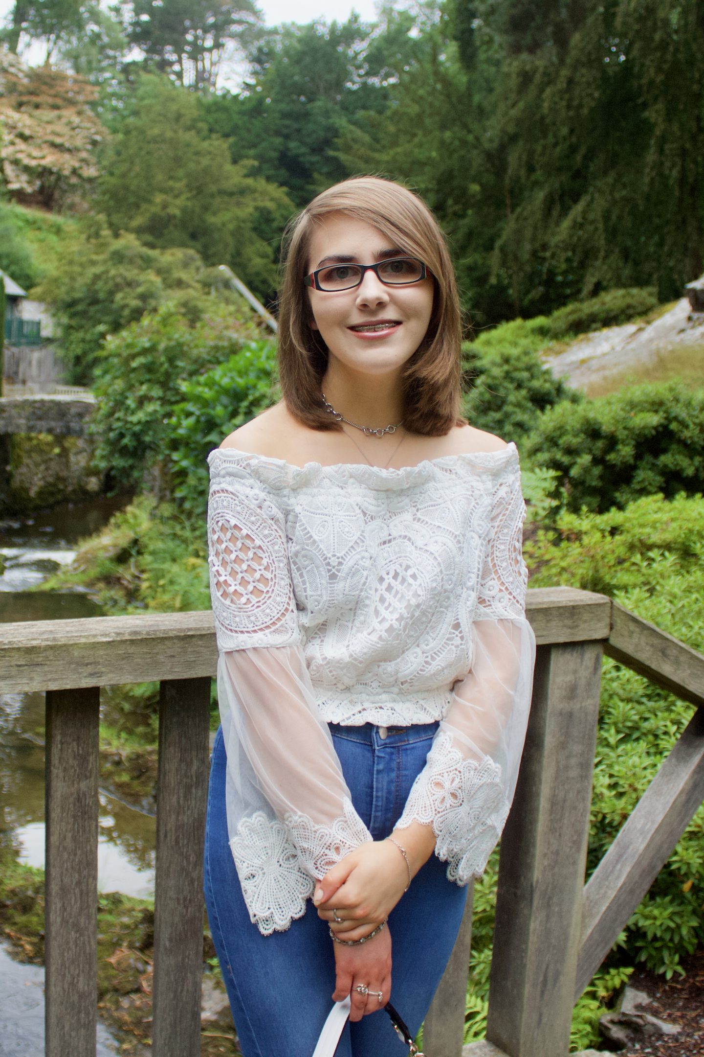 From 20 to 21: A photo of Elin standing on a wooden bridge with trees and flowers in the background