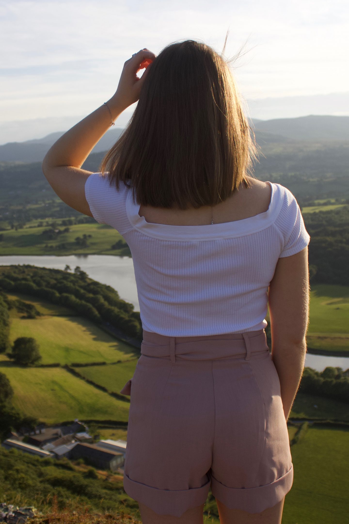 A photo of Elin from the back, she is looking out at a view of mountains, fields and a river
