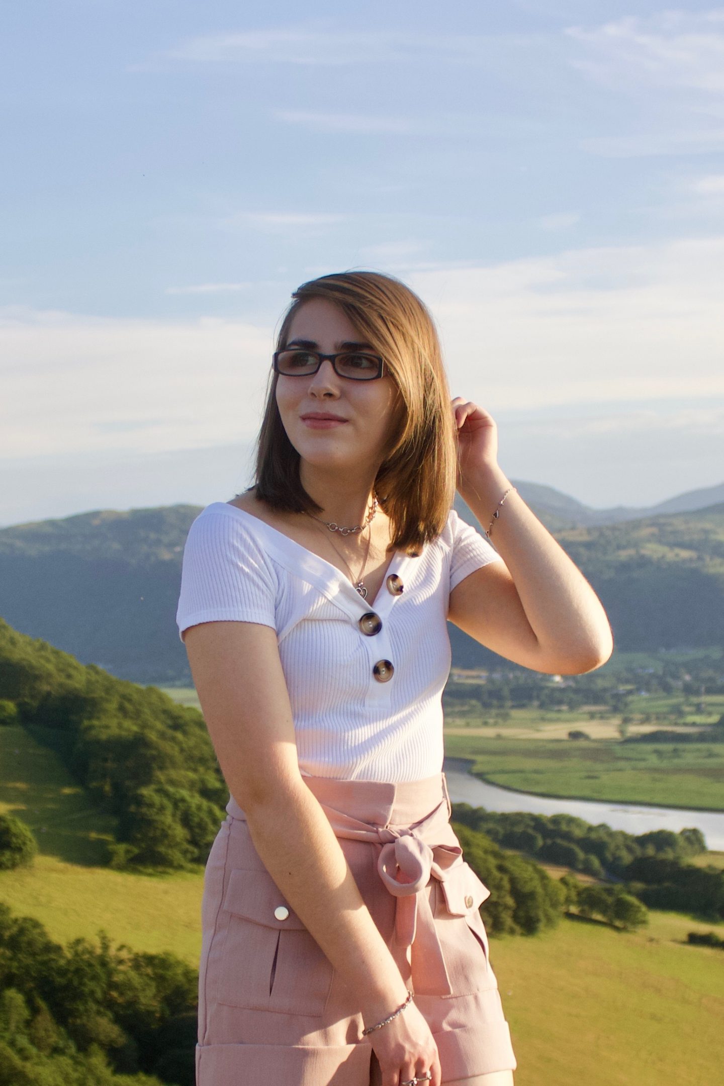 The fear of missing out as a blind person in a visual world: A photo of Elin looking away to the right, her hand is raised to her hair and there are mountains to be seen in the background
