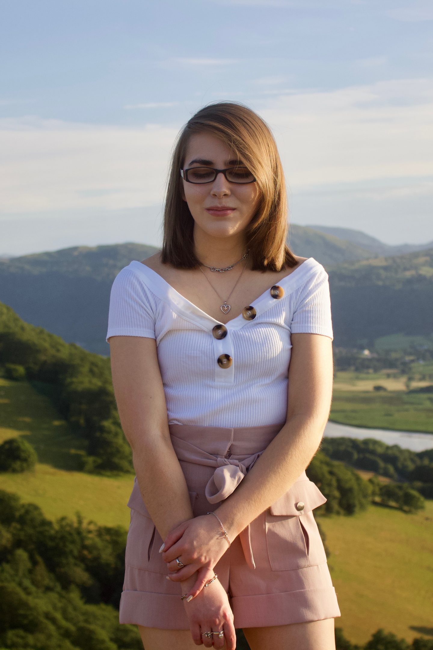 A photo of Elin looking down, she stands in front of a view of mountains and fields