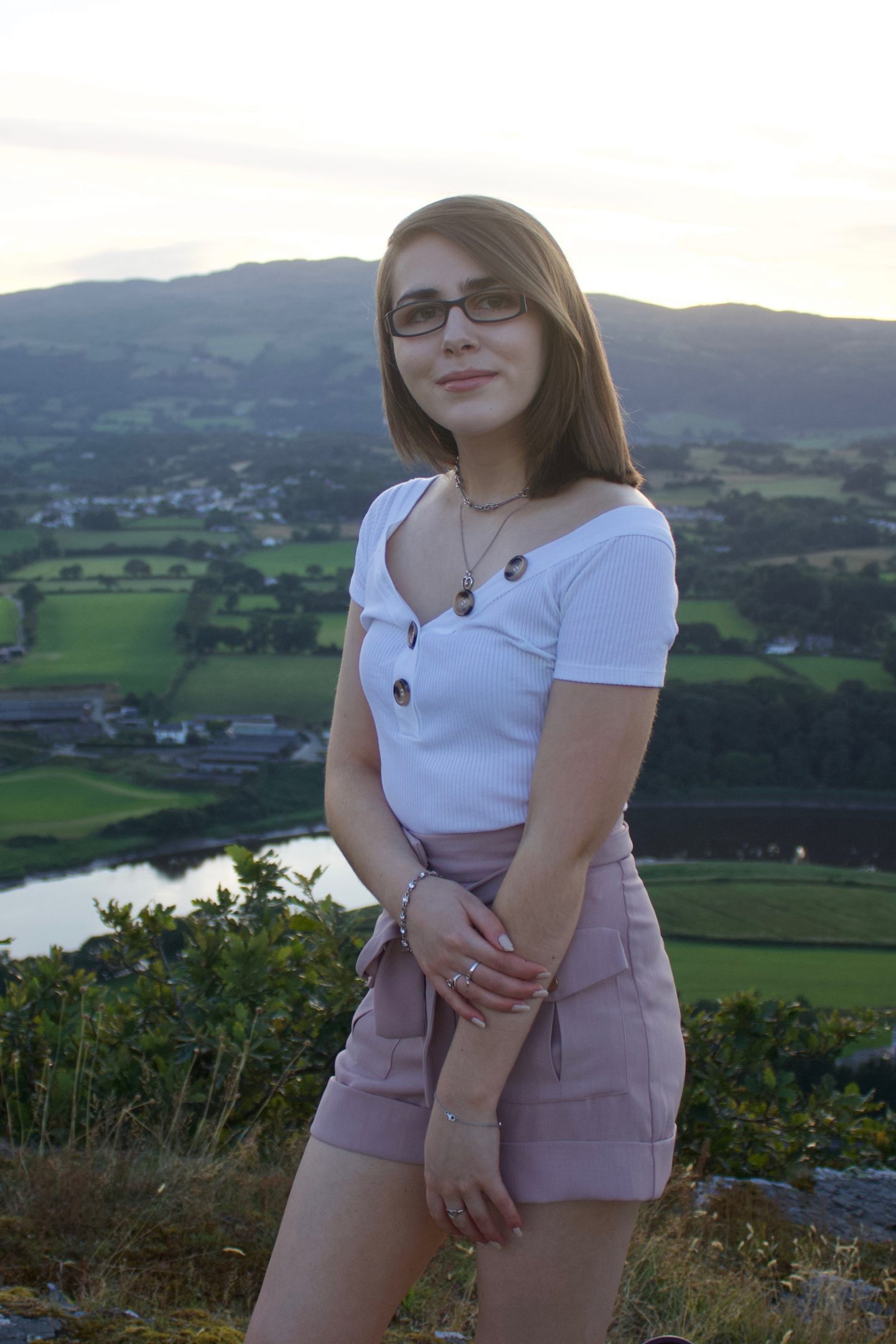 A photo of Elin from the side, she is wearing a white bardot top which has buttons on the neckline and high waisted pink utility shorts