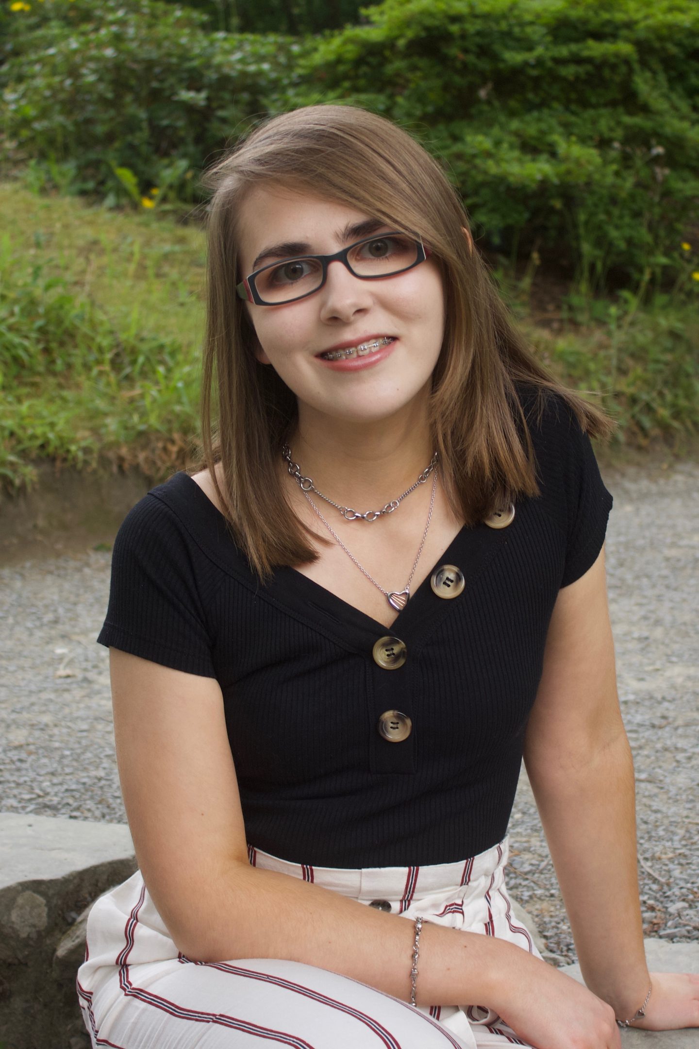 A photo of Elin crouching down, there are plants and trees in the background