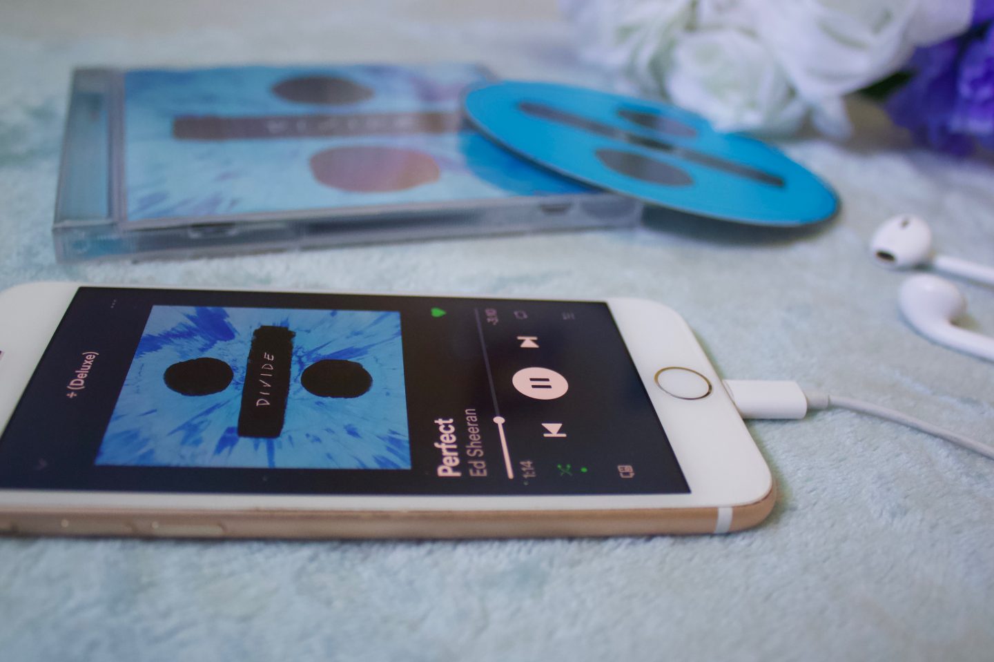 A photo of the song Perfect playing on my phone, my earphones are plugged into it and the album and CD can be seen in the background which is out of focus