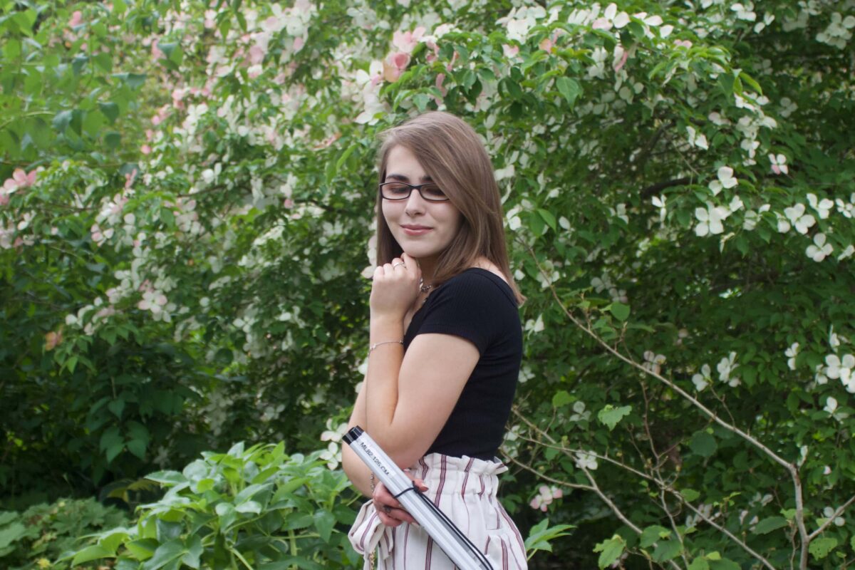 A photo of Elin from the side, she is holding her folded up cane in one of her hands and she is looking down