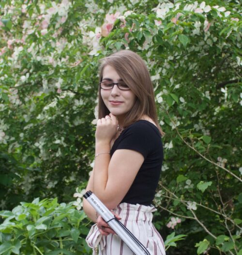 A photo of Elin from the side, she is holding her folded up cane in one of her hands and she is looking down