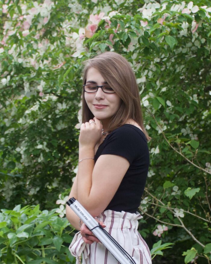 A photo of Elin from the side, she is holding her folded up cane in one of her hands and she is looking down