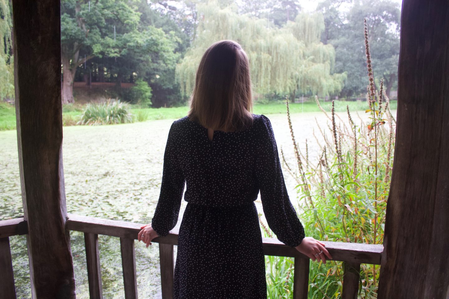 A photo of Elin standing in a wooden boathouse, the photo is taken from the back as she looks out on the small lake