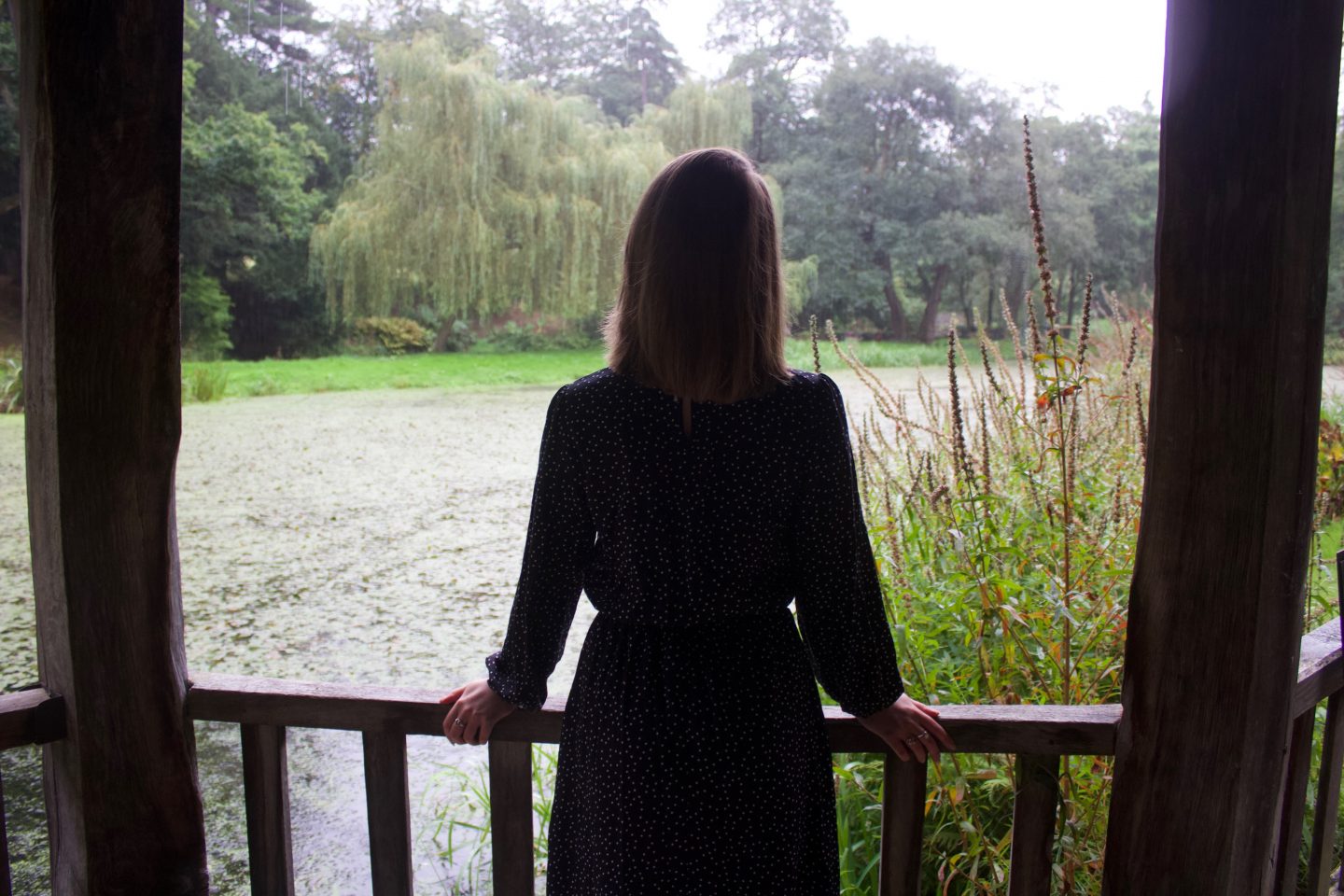 A photo of Elin standing in a wooden boathouse, the photo is taken from the back as she looks out on the small lake