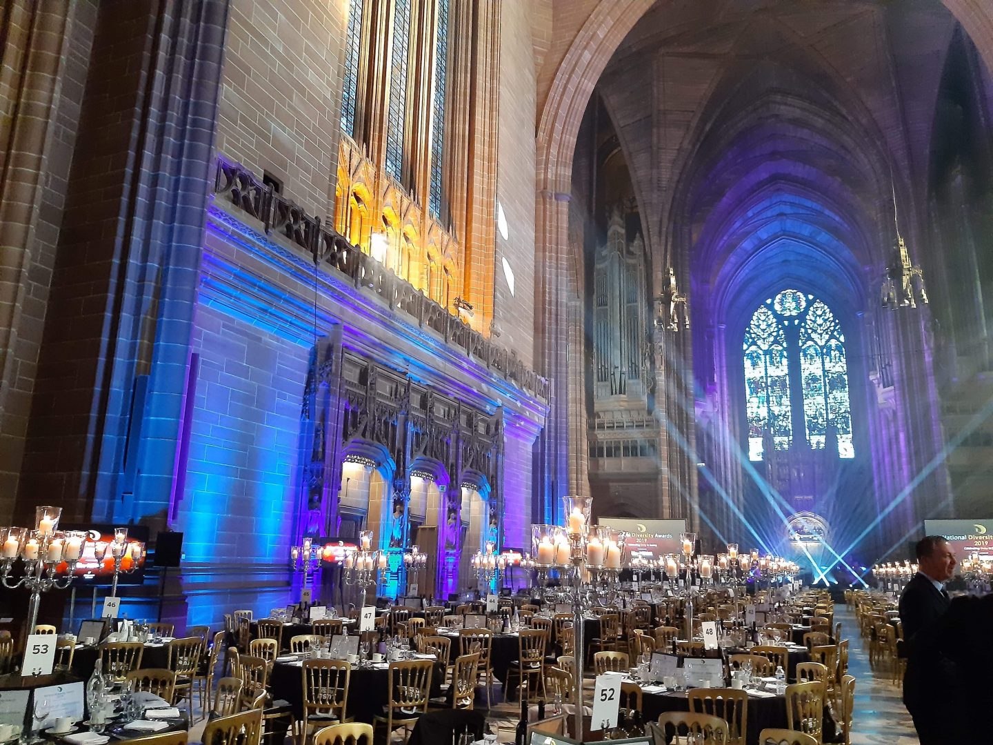 A photo of the tables extending towards the pretty east window, a pretty blue light is cast over them.
