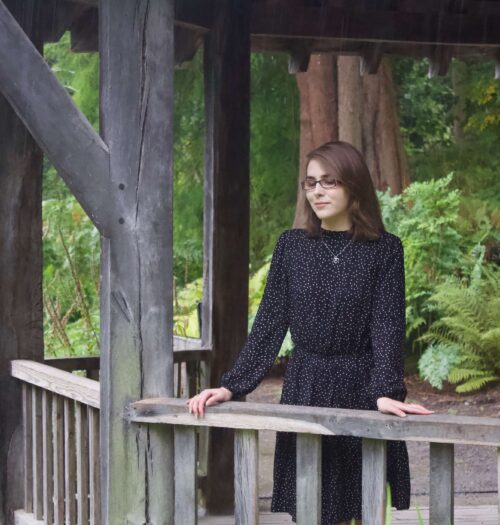 A photo of Elin standing in a wooden boat house, she is leaning on the fence and looking down