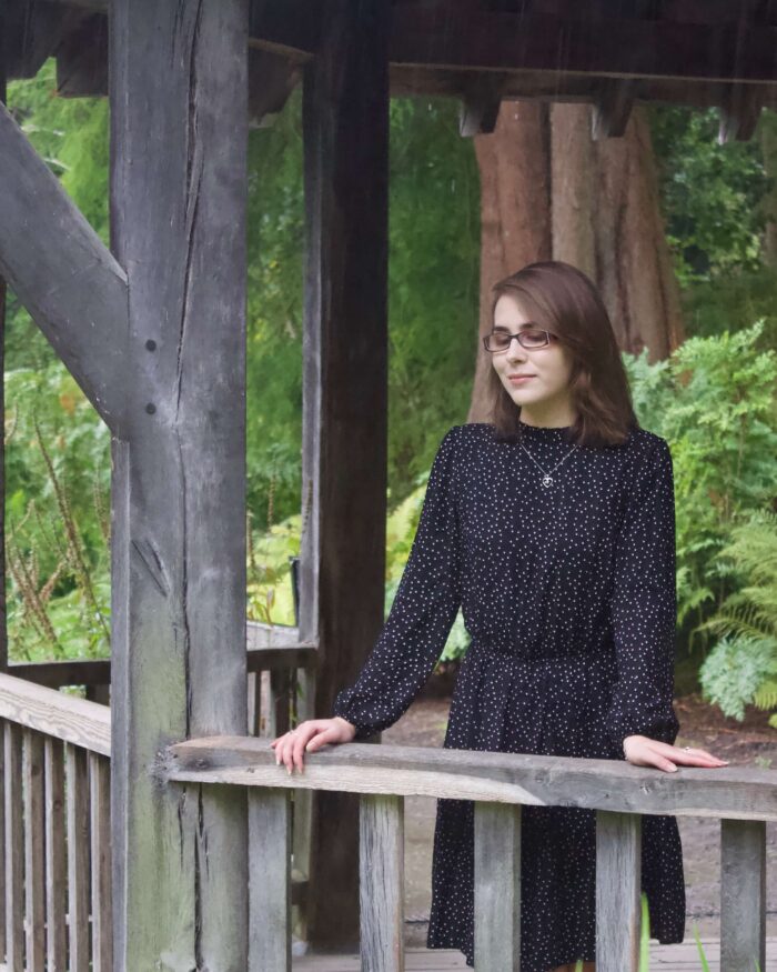 A photo of Elin standing in a wooden boat house, she is leaning on the fence and looking down