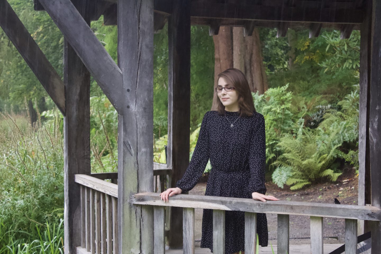 A photo of Elin standing in a wooden boat house, she is leaning on the fence and looking down