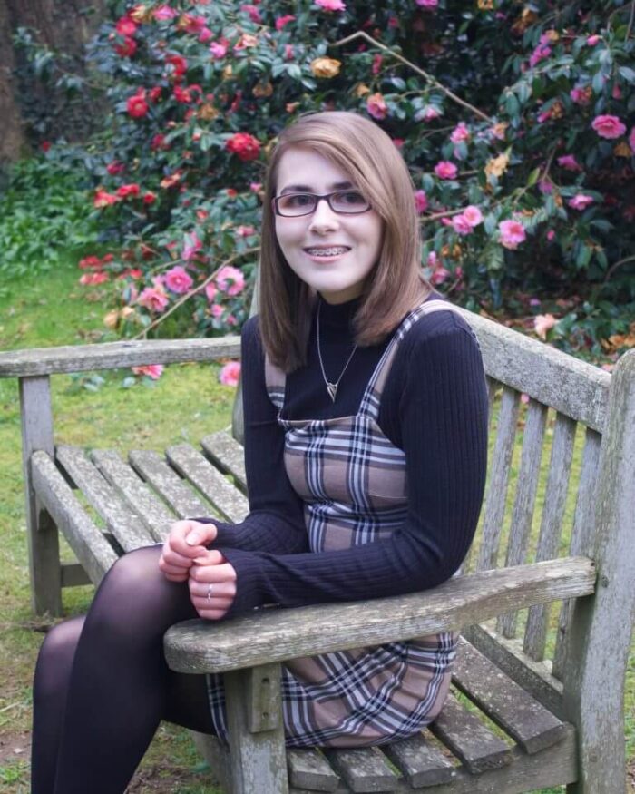 A photo of Elin sitting on a bench, there are pink flowers in the background
