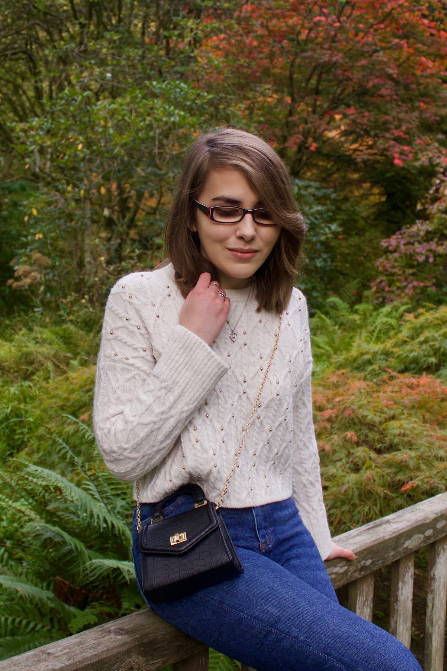A photo of Elin sitting on a wooden bridge, her right hand is raised to hold the ends of her hair and she is looking down
