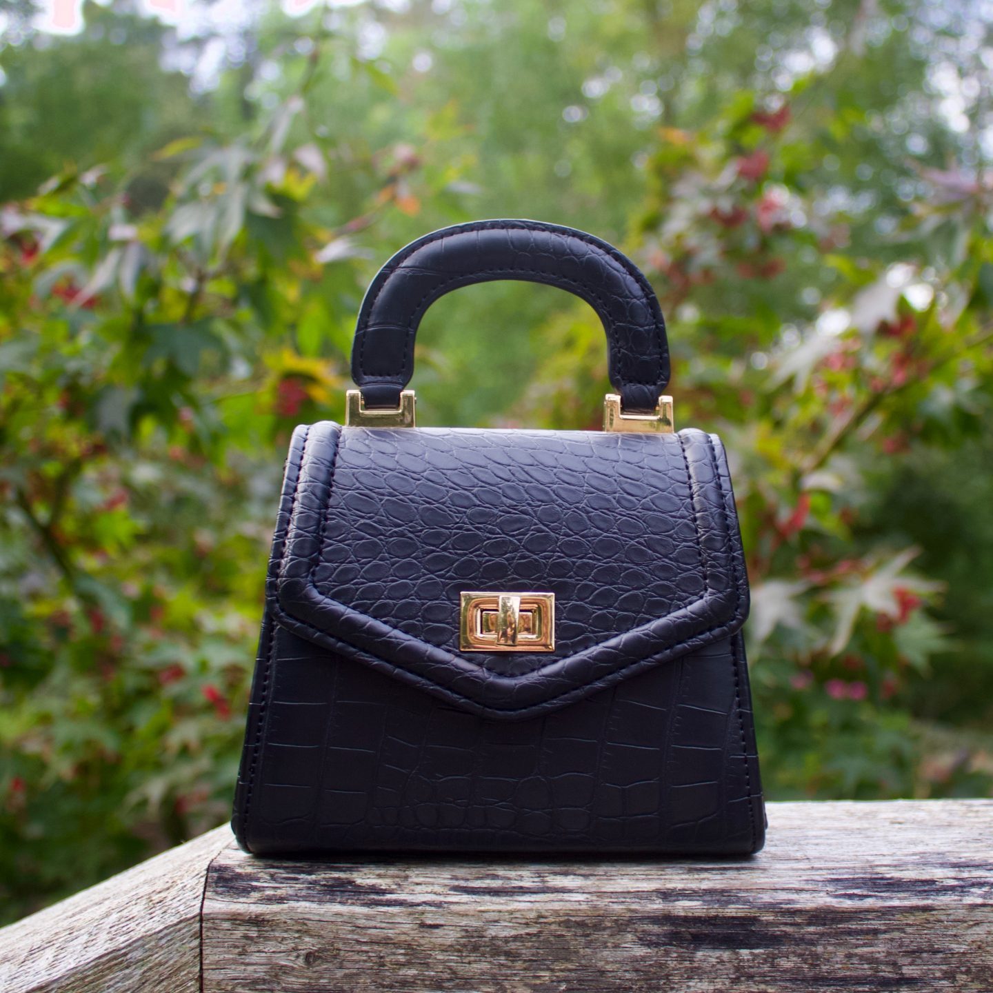 A photo of a small black bag which has croc detailing on it, there's a tiny handle on the top.