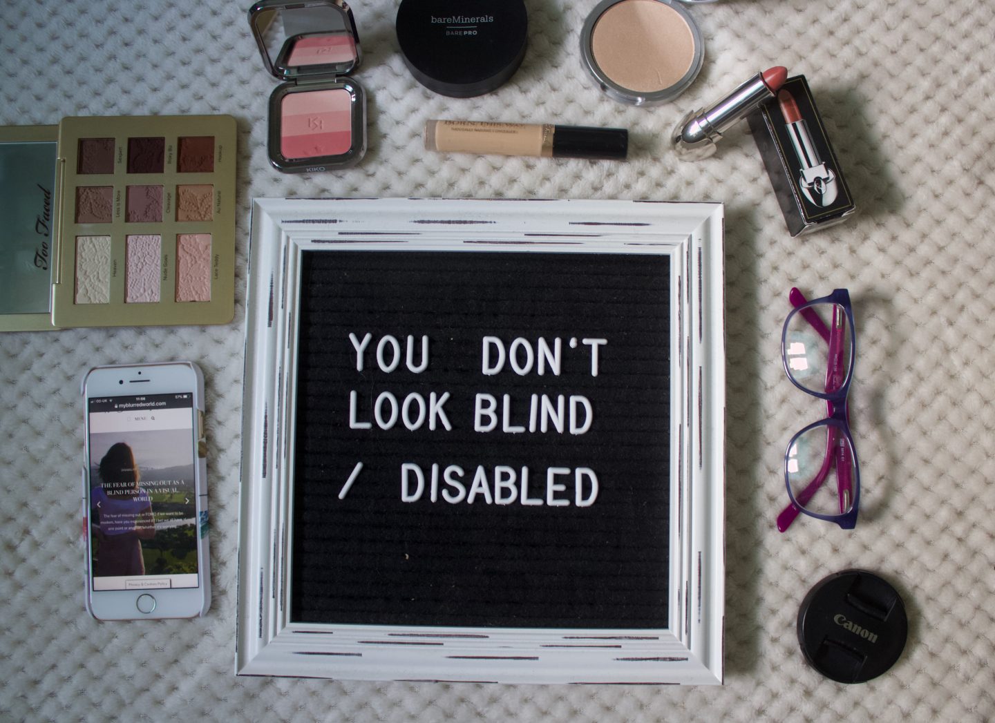A photo of a black felt letter board with a thick white vintage frame, my phone is beside it with my blog's homepage showing on it, glasses are on the other side and there are makeup products around it too