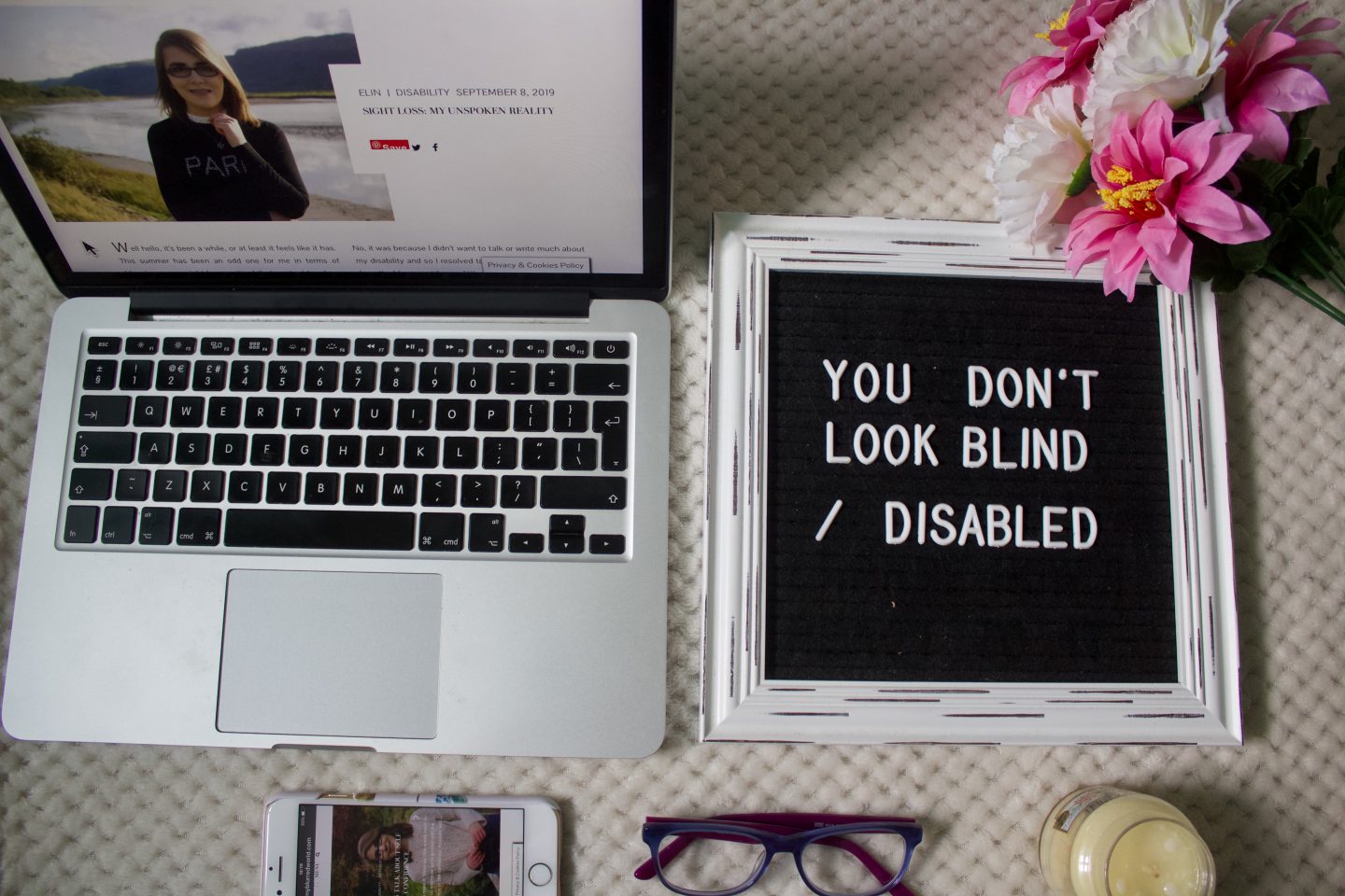A photo of one of my blog posts on a macbook screen, there's a felt letter board beside it which says you don't look blind/disabled, the board has a vintage white frame