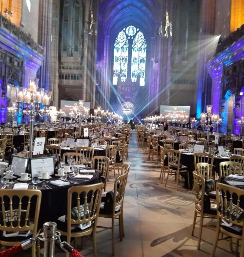 A photo of the tables set out for the awards, a pretty window can be seen at the end above the lights of the stage