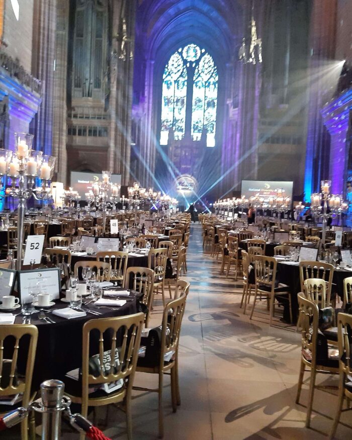 A photo of the tables set out for the awards, a pretty window can be seen at the end above the lights of the stage