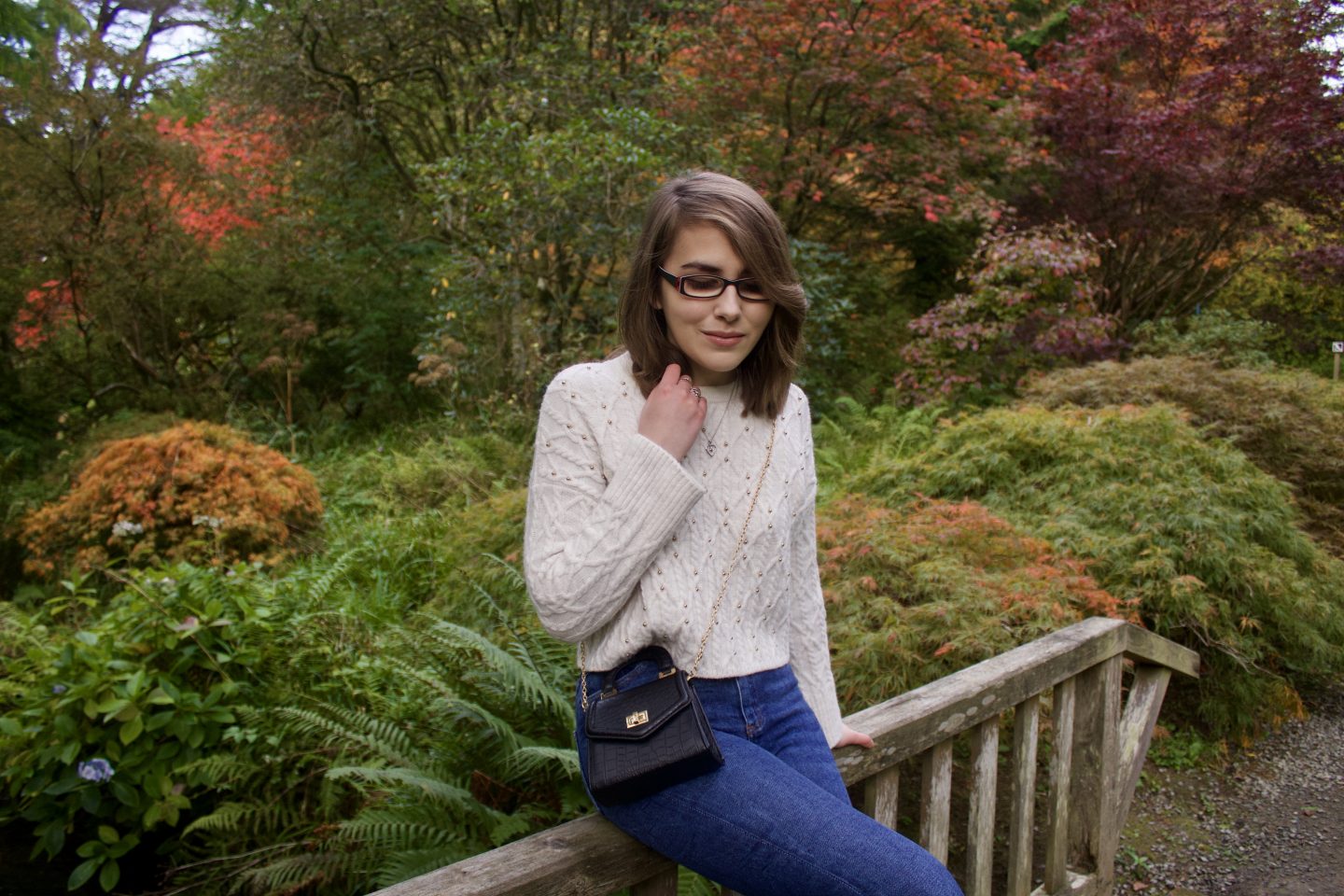 A photo of Elin sitting on a wooden bridge, her right hand is raised to hold the ends of her hair and she is looking down