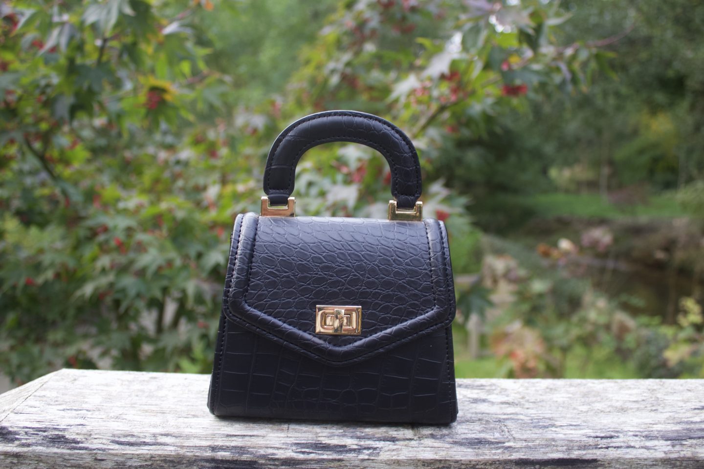 A photo of a small black bag which has croc detailing on it, there's a tiny handle on the top.