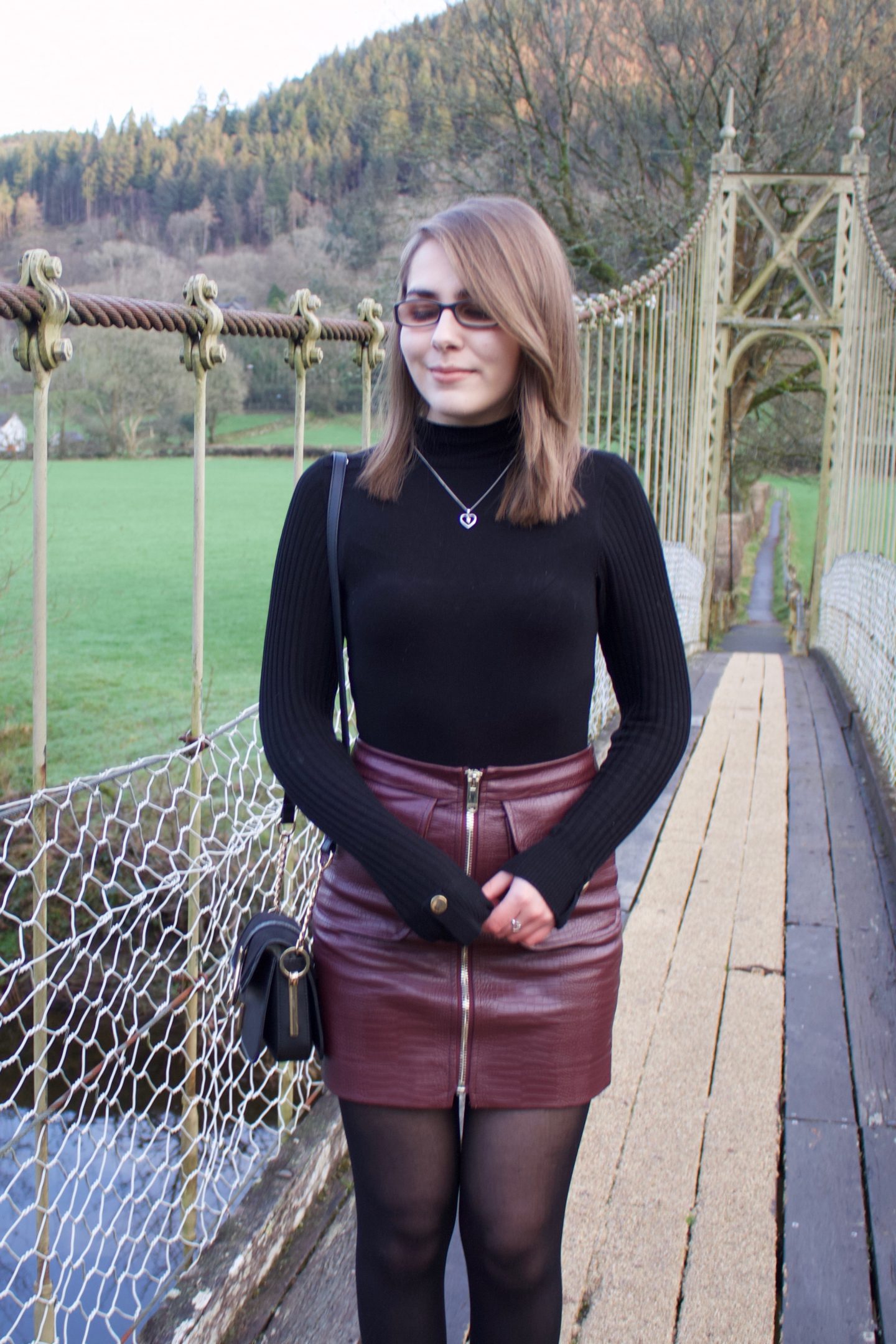 A photo of Elin standing on a suspension bridge, a mountain can be seen in the background and she's looking down