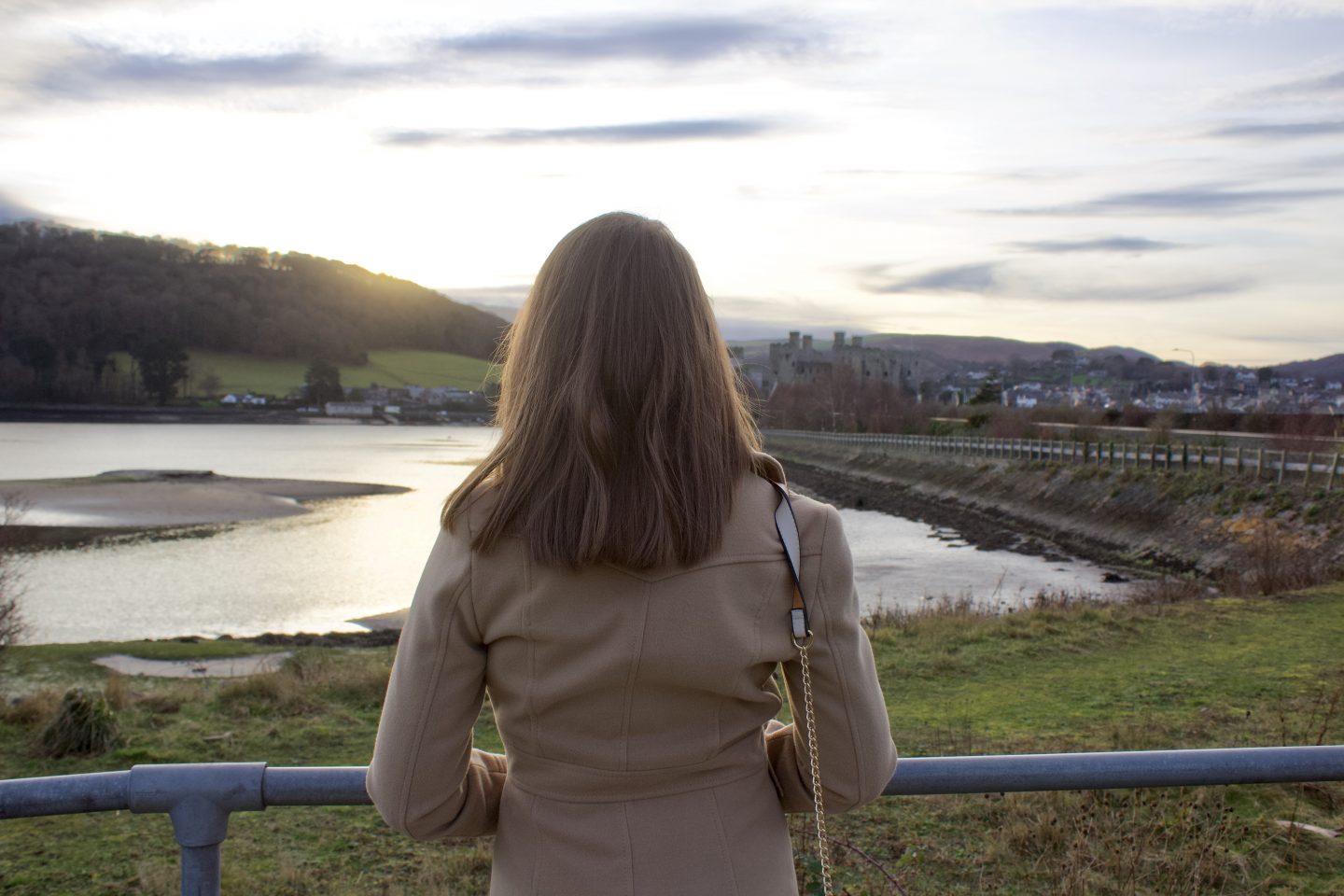 A photo of Elin from the back looking out on a river. The castle can be seen in the distance.