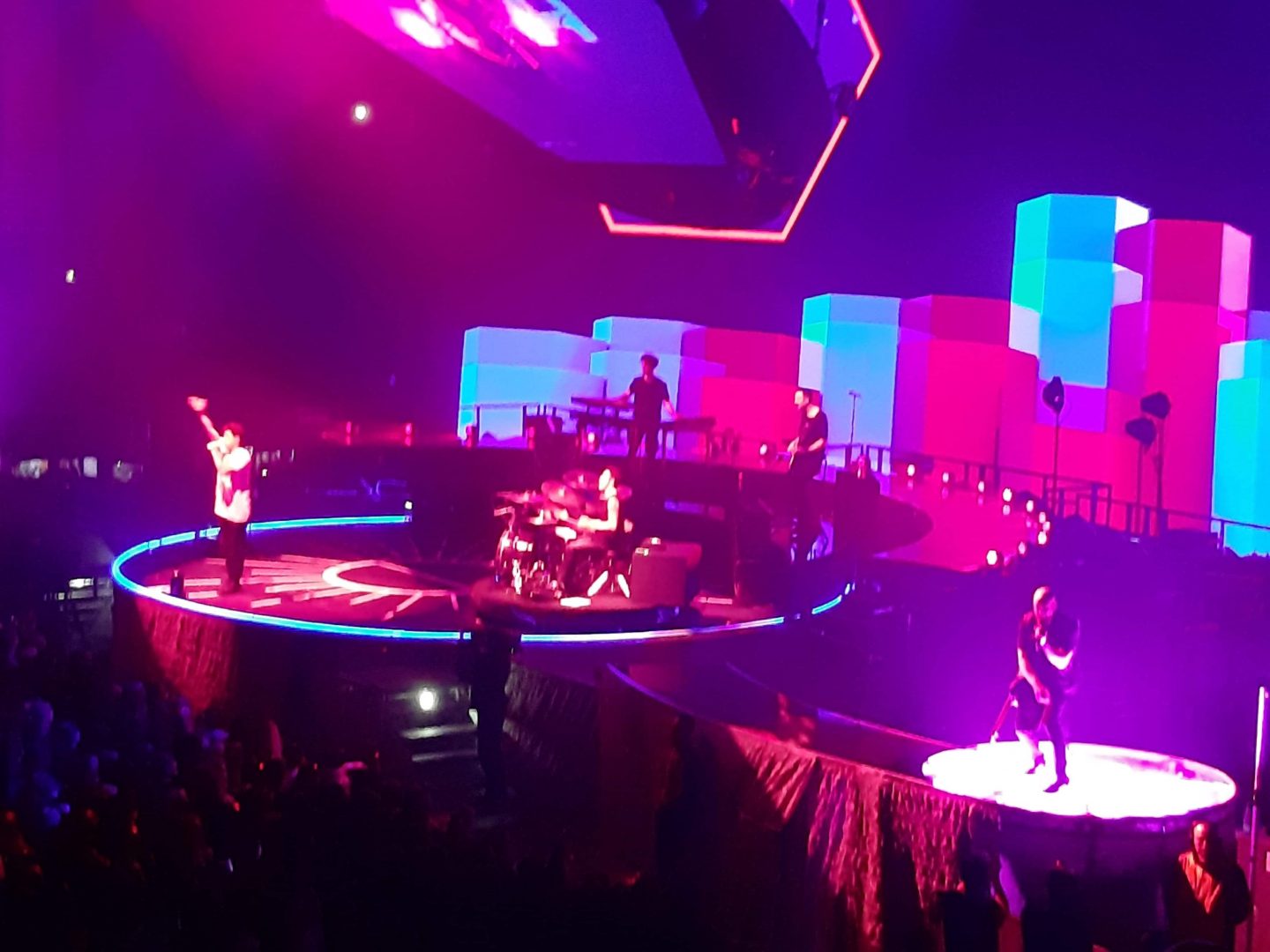 A photo of The Scriipt on stage at Manchester Arena. The stage and its background are really colourful with pink and blue being the main colours you can see