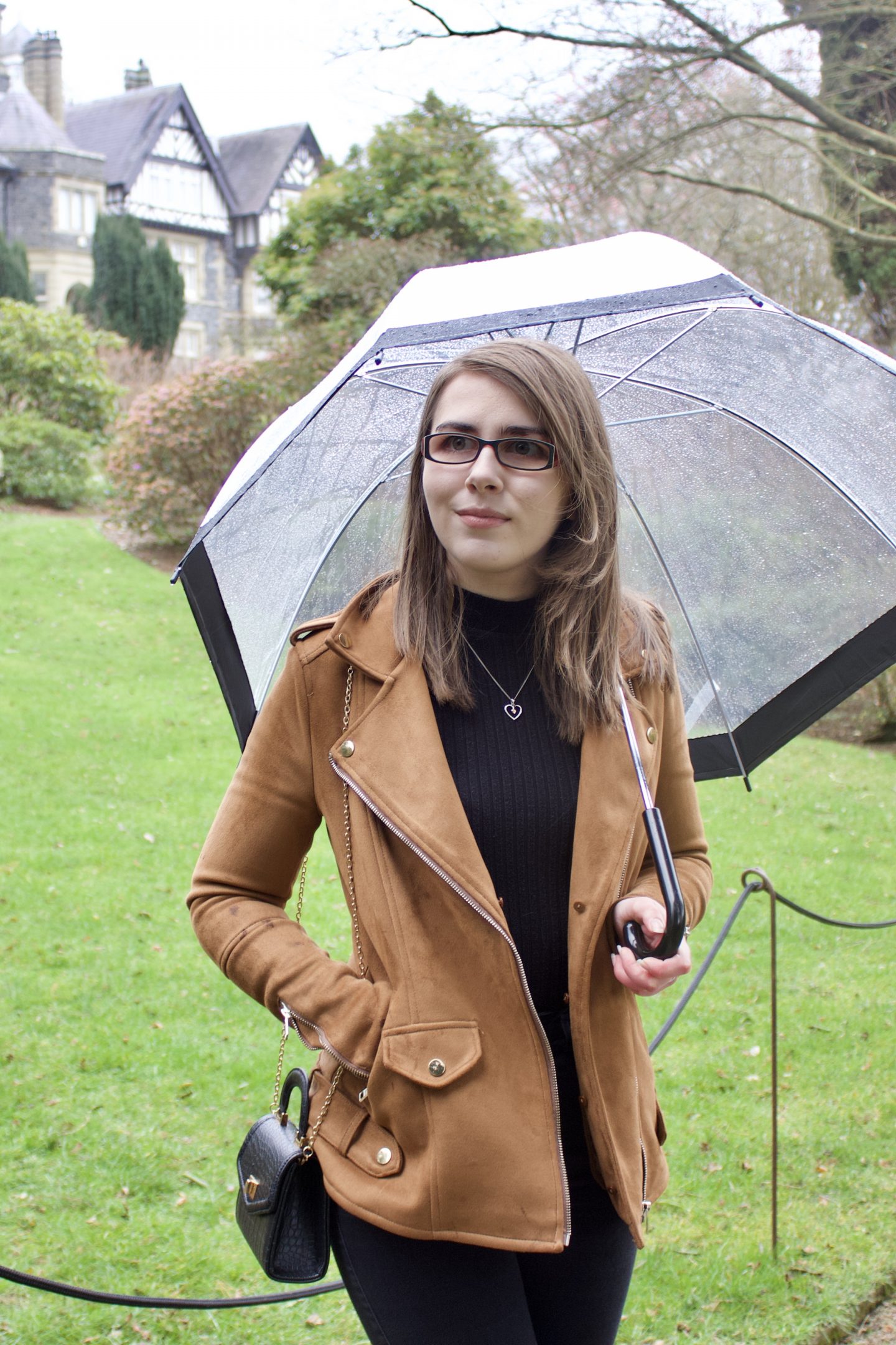 A photo of Elin standing on a lawn with a tudor style house peeking out in the background, she's looking away from the camera