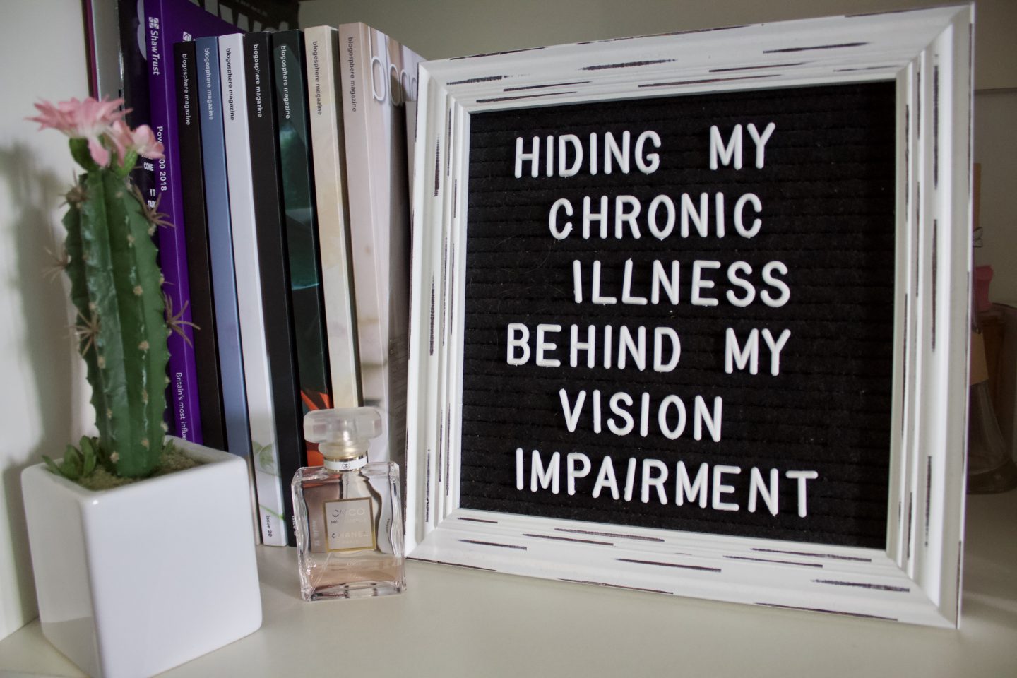 A photo of the white framed black letter board which displays the blog post title on it, there's a small Chanel perfume standing in front of the bottom left corner of the frame and a fake cactus beside it in a small square shaped white pot