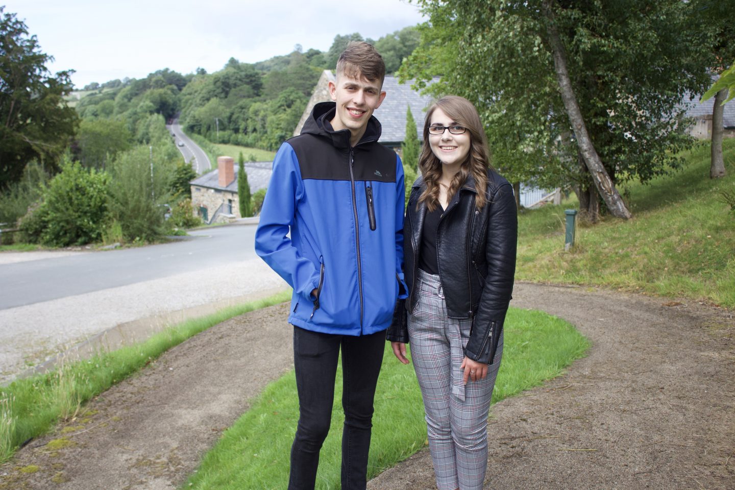 A photo of my brother and I standing on a footpath with trees on the right hand side. We're both smiling at the camera