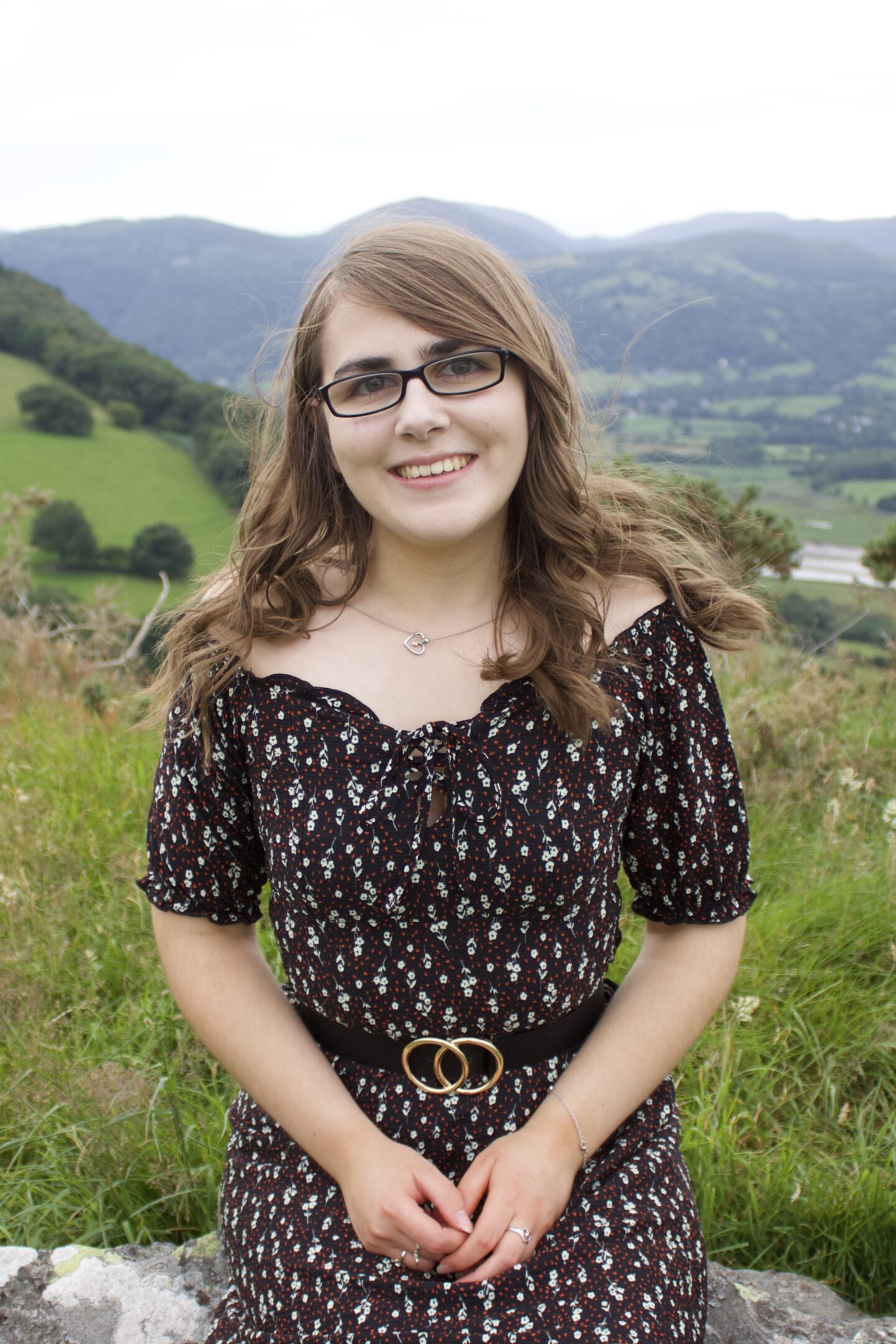 A photo of Elin sitting on a rock in front of a view of mountains, she's smiling widely at the camera