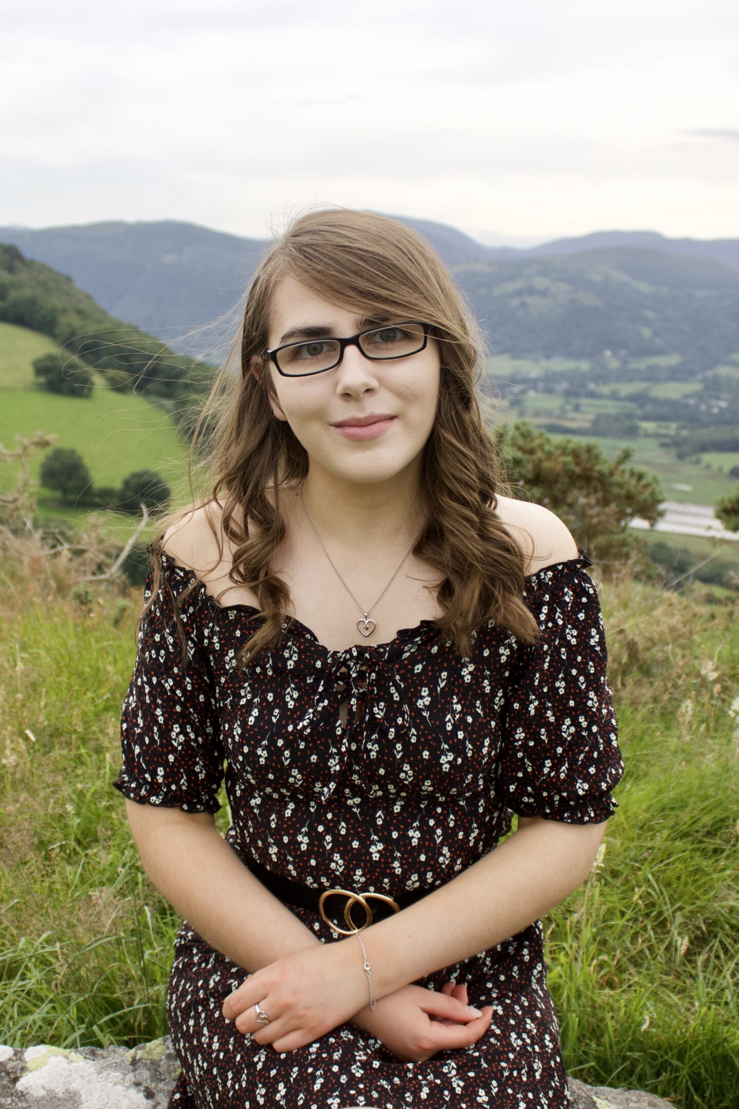 A photo of Elin sitting on a rock with fields and mountains in the background,