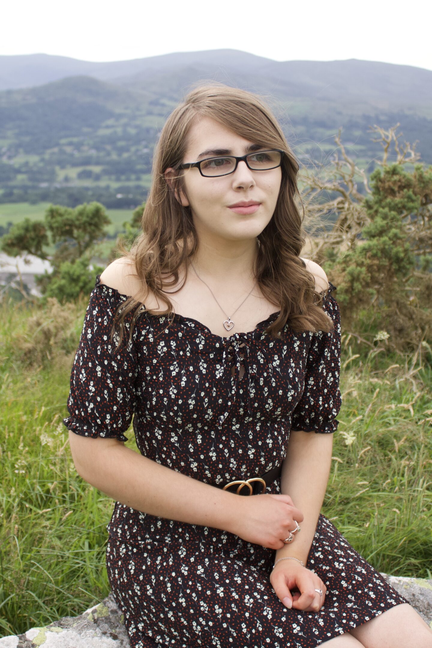 A photo of Elin sitting on a rock in front of a view of mountains, she's looking away from the camera