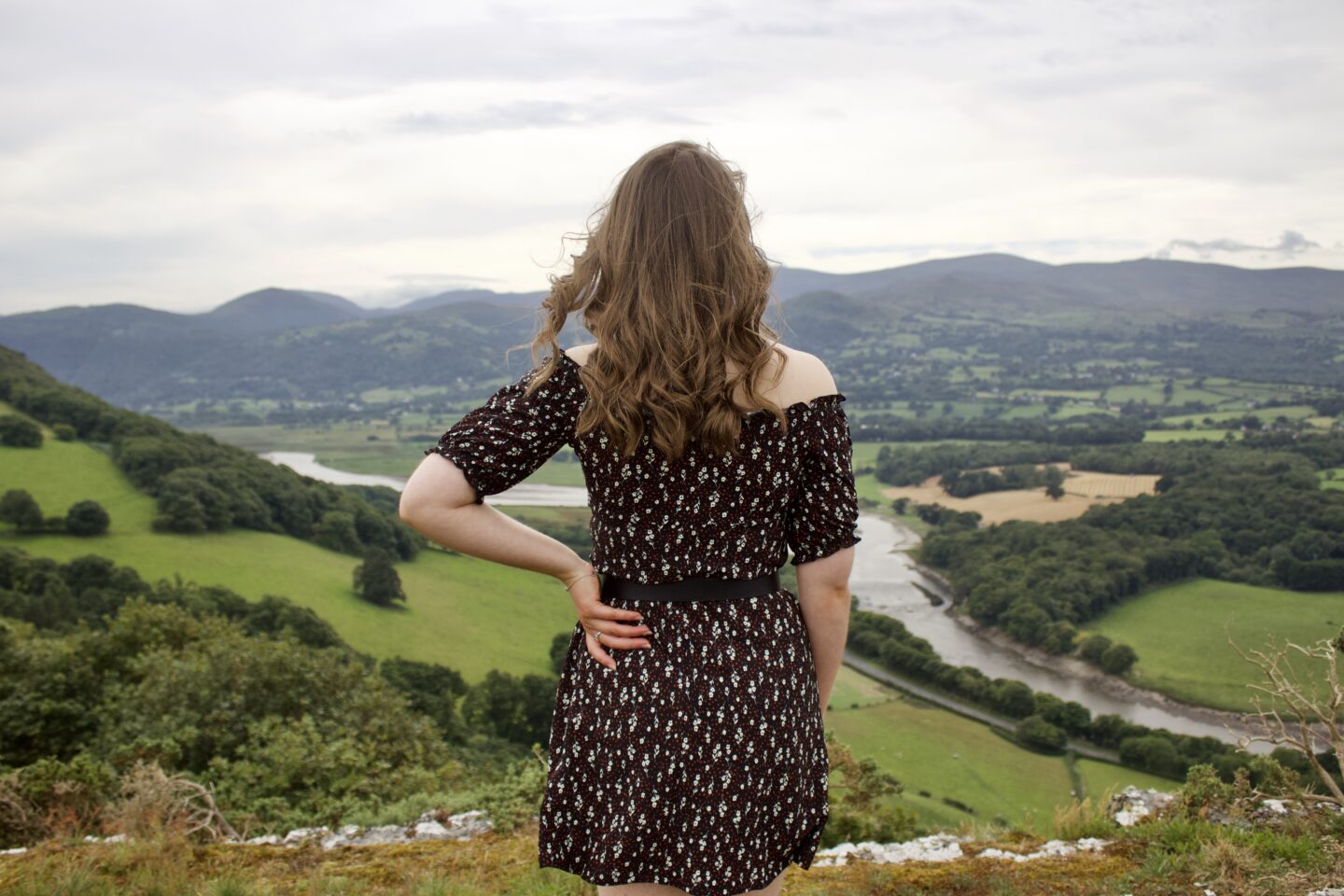 A photo of Elin from the back, looking over a view of fields, mountains and a river
