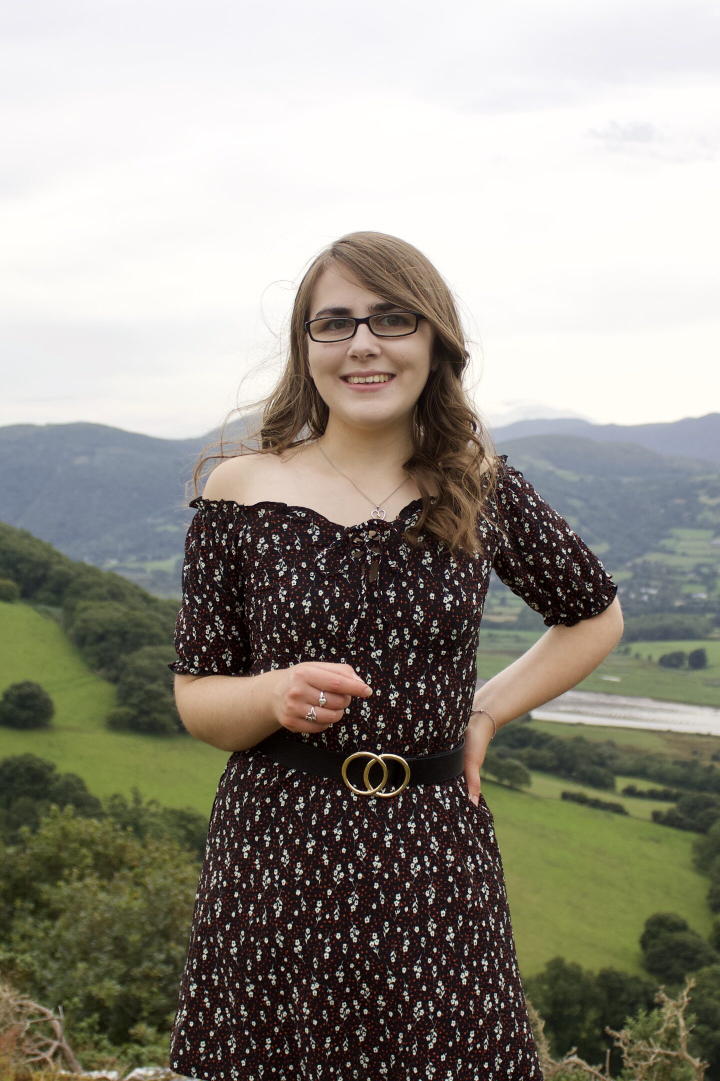 A photo of Elin in front of a view of mountains, she's smiling at the camera and her left hand rests on her hip