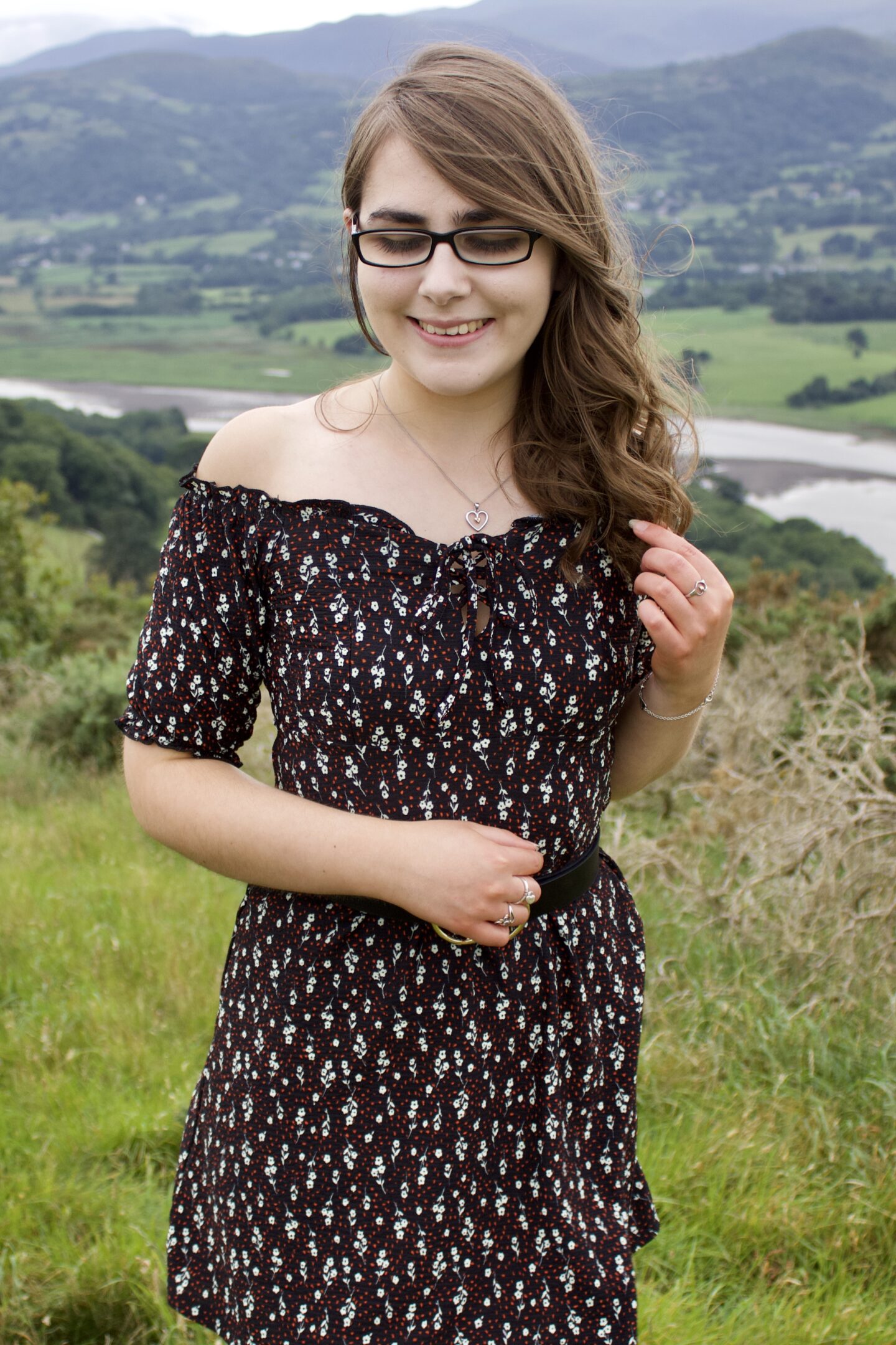 A photo of Elin with mountains in the background. She's looking down and smiling. Her left hand holds a strand of her long hair
