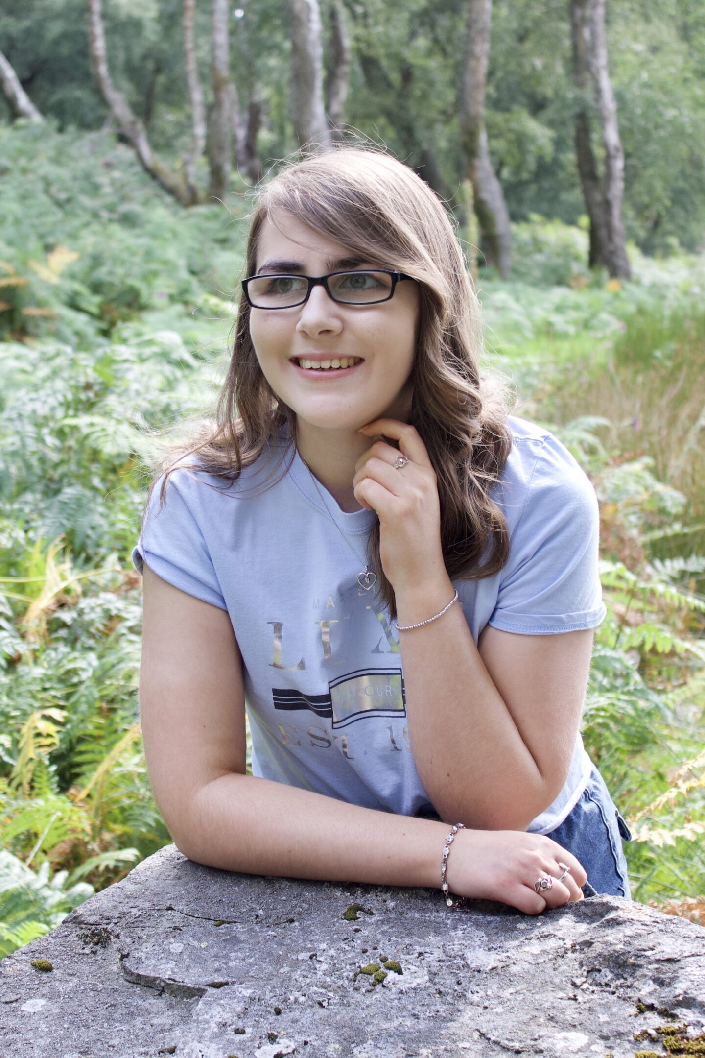 A photo of Elin leaning forward on a rock, her left arm is raise to just underneath her chin and she's looking away from the camera, smiling