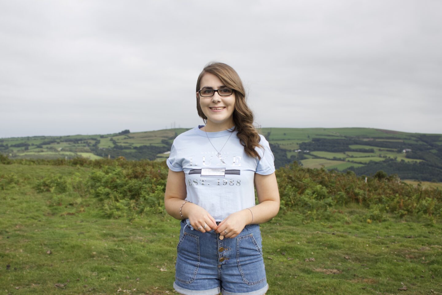 A photo of Elin wearing a light blue cropped t-shirt with high waisted denim shorts, she's smiling at the camera