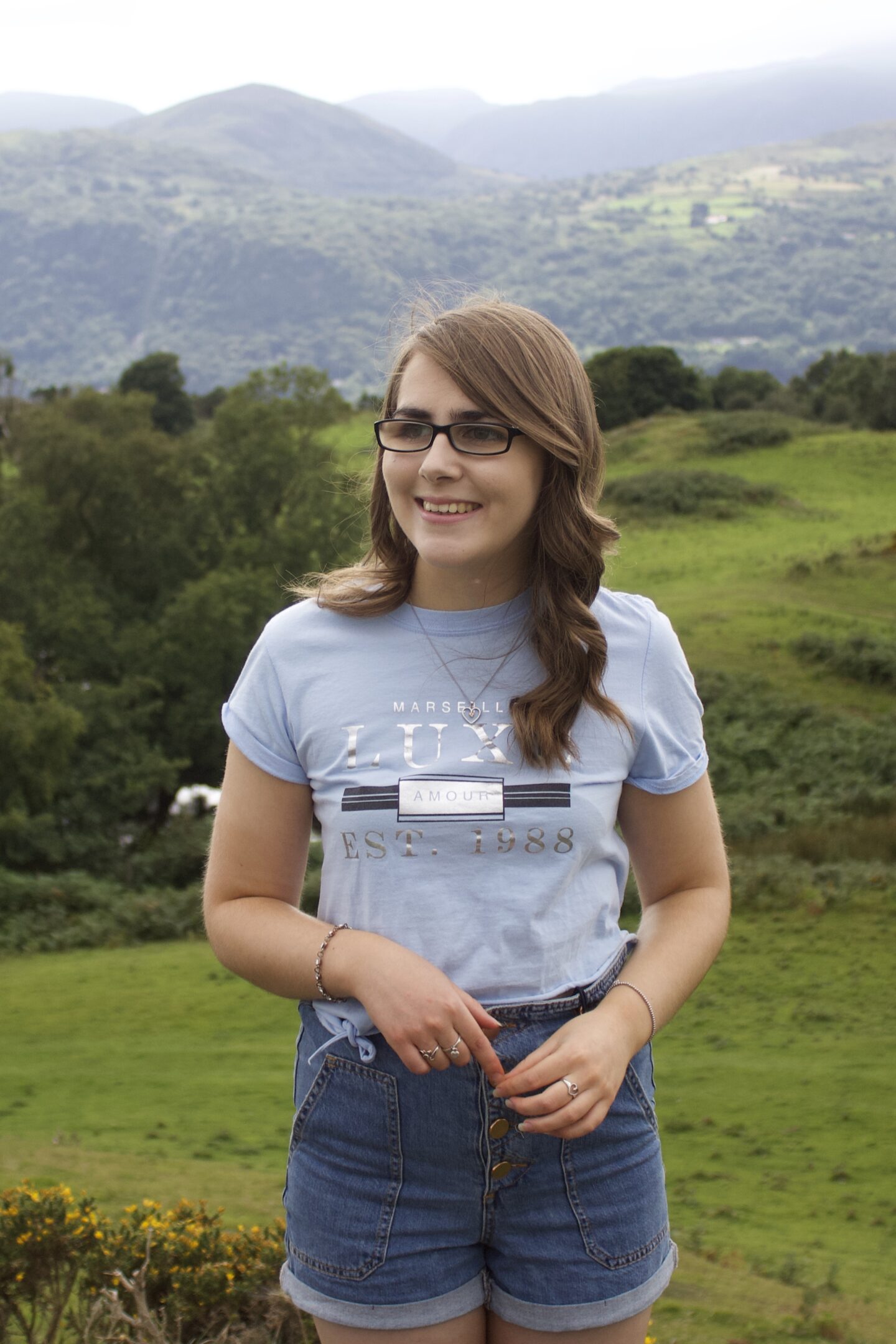 A photo of Elin standing in front of a view of mountains, she's smiling and looking away from the camera.